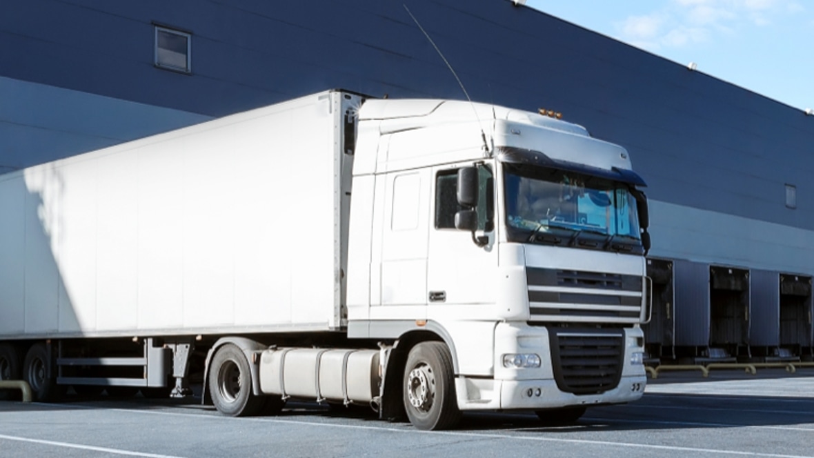 Image shows a white truck full of goods outside a closed indoor warehouse.